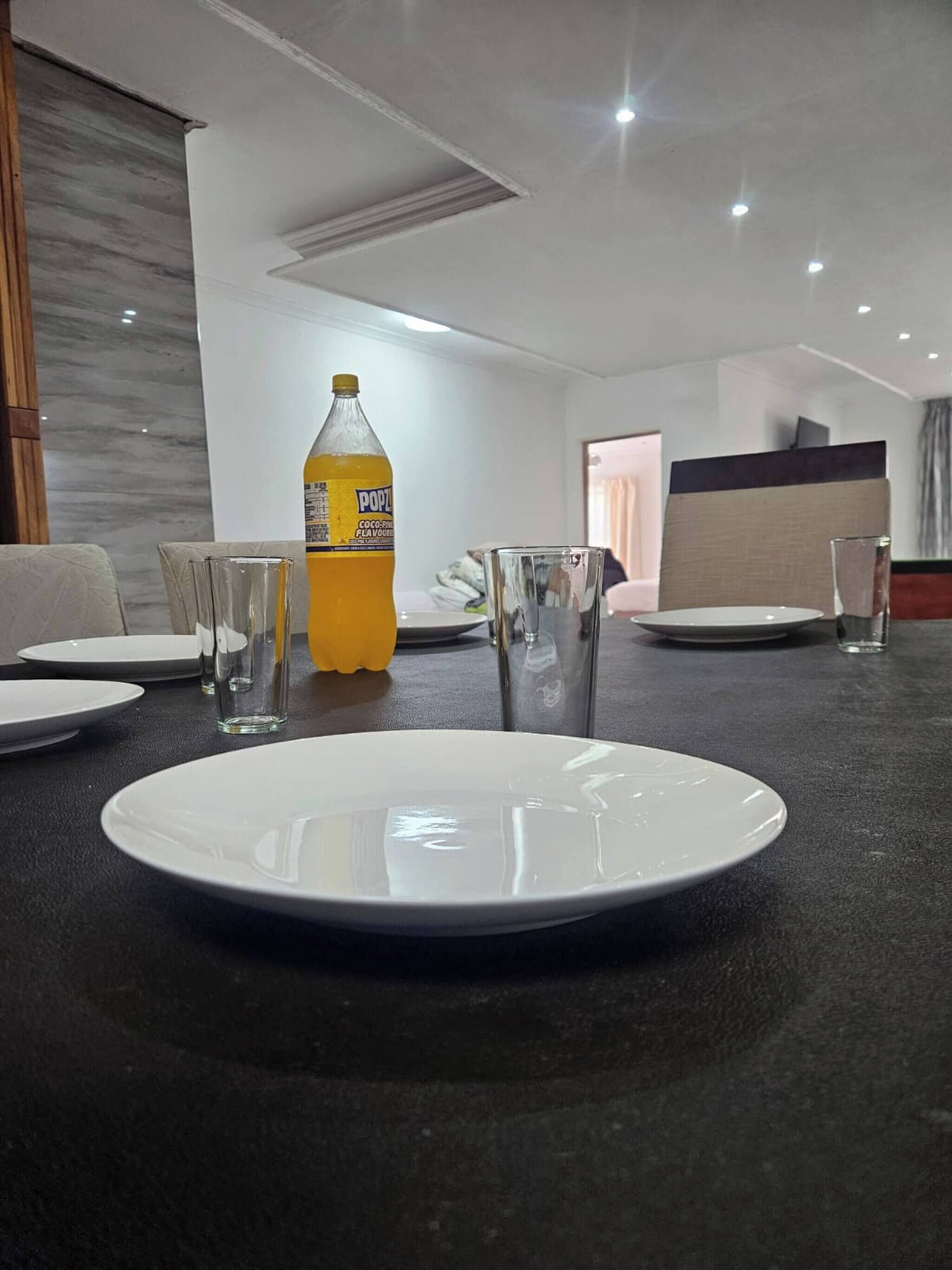 A dining table with plates, glasses, and a bottle of soda.