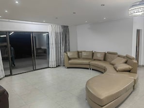 A modern living room with a curved sofa, a glass door leading to a balcony, and a tiled floor.
