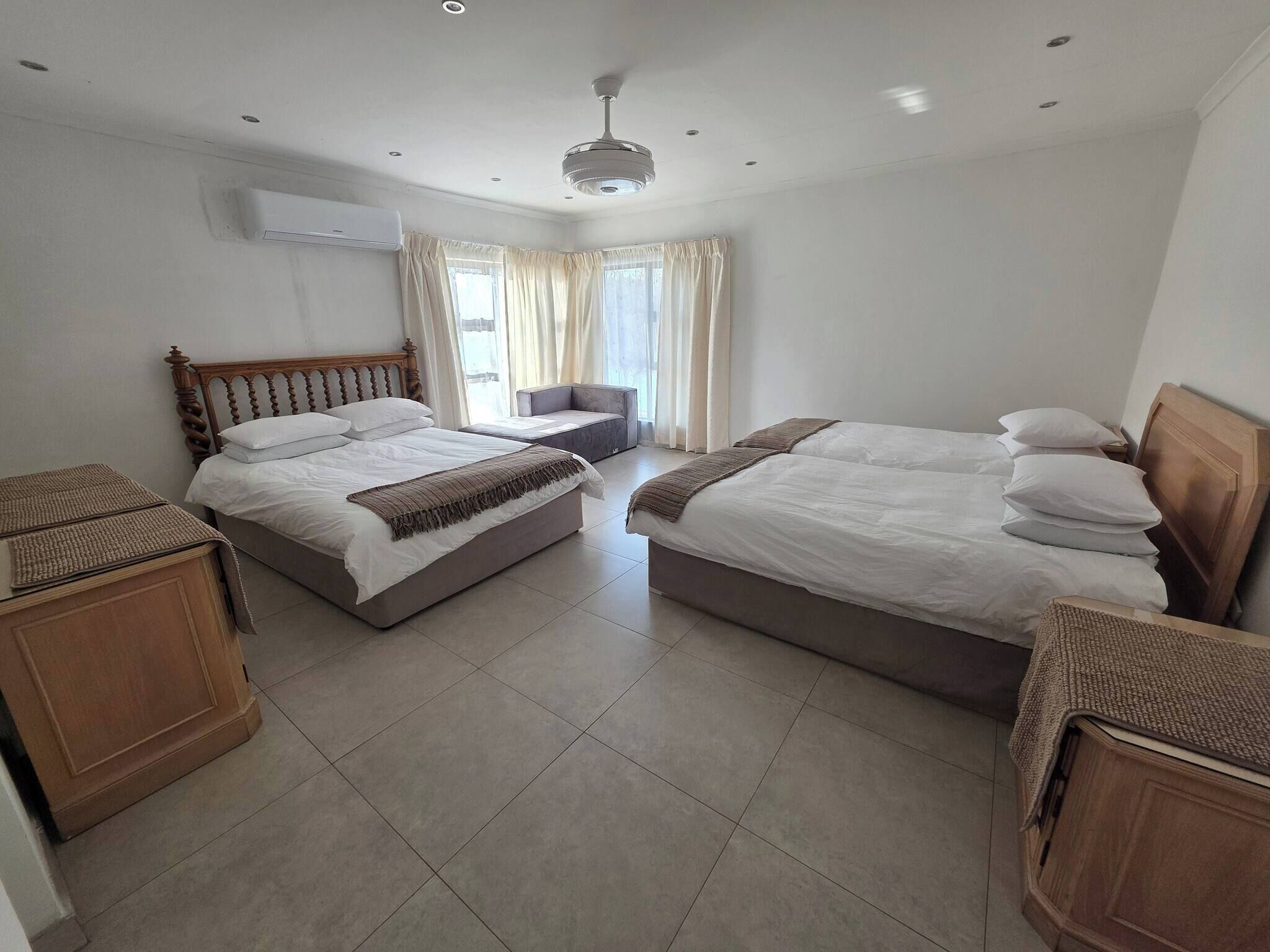 Habitación de hotel con dos camas, un sofá, un armario de madera y un equipo de aire acondicionado.