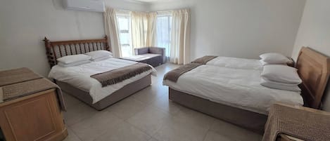 Habitación de hotel con dos camas, un sofá, un armario de madera y un equipo de aire acondicionado.