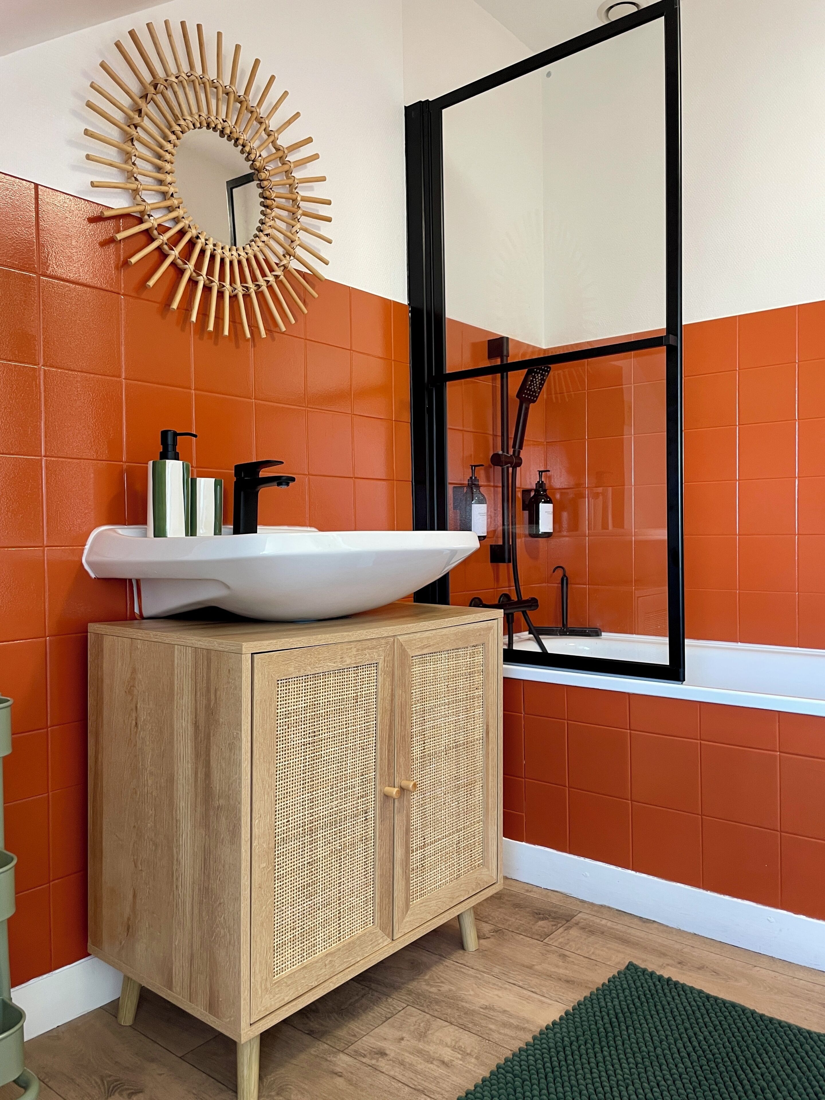 A bathroom with a wooden cabinet, a large mirror, and orange tiles.