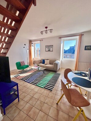 Una sala de estar con un sofá, una mesa de centro, un televisor, un tapete estampado y una escalera.