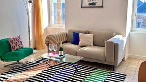 A living room with a sofa, a glass coffee table, a colorful striped rug, and a framed sign on the wall. - Colorful 3-bedroom apartment in the heart of downtown with outdoor space (La Gacilly)