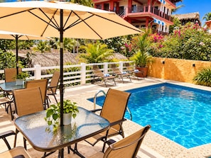 A poolside area with lounge chairs, a table with chairs, and a large umbrella. - Casa piedra parada hotel (Brisas de Zicatela)