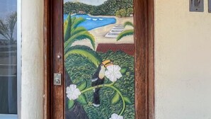 Una puerta con un mural pintado de un paisaje, el número 18 encima y un enchufe pequeño a la derecha.