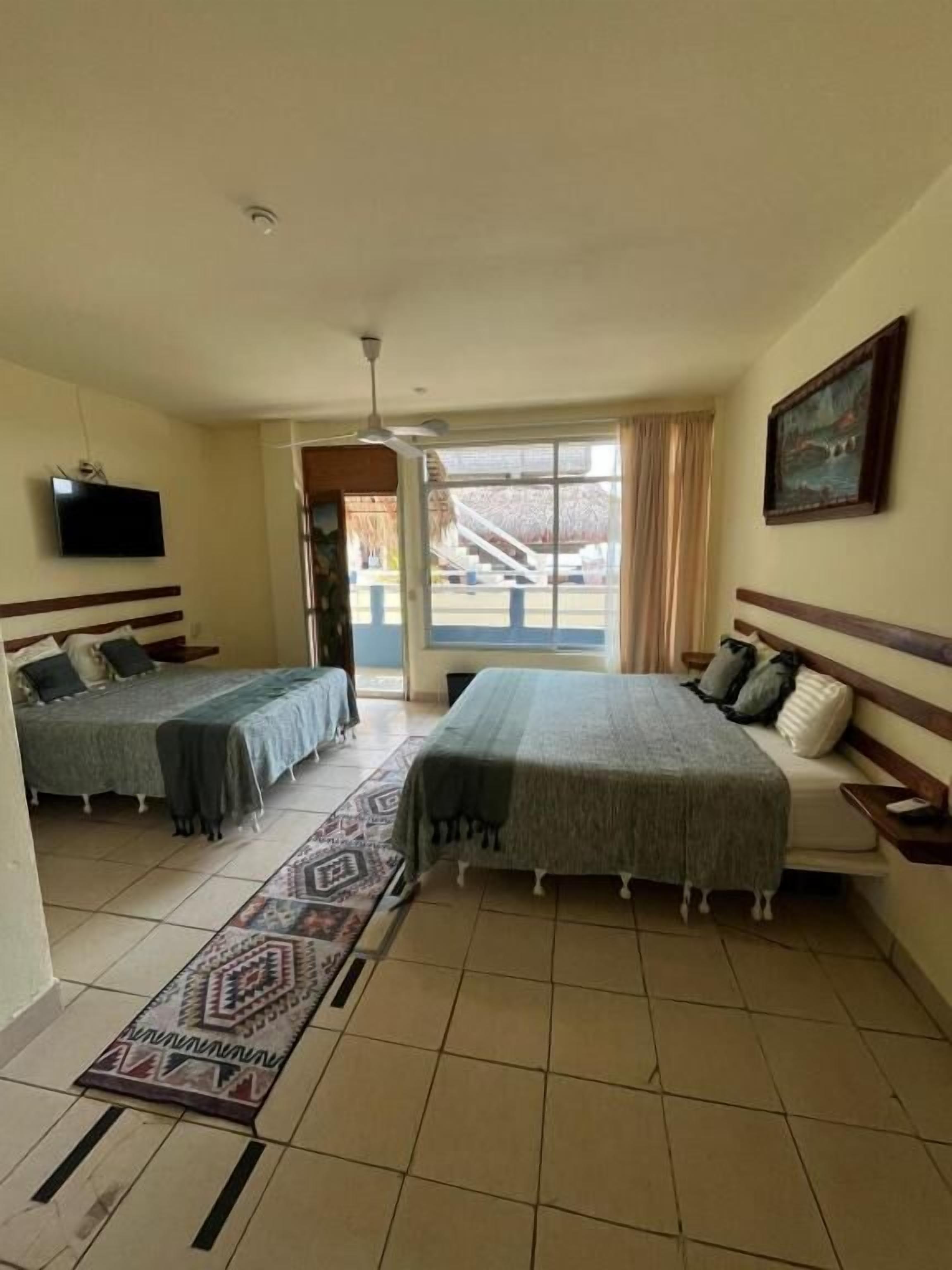 A hotel room with two beds, a TV, a painting, and a view of the outside.