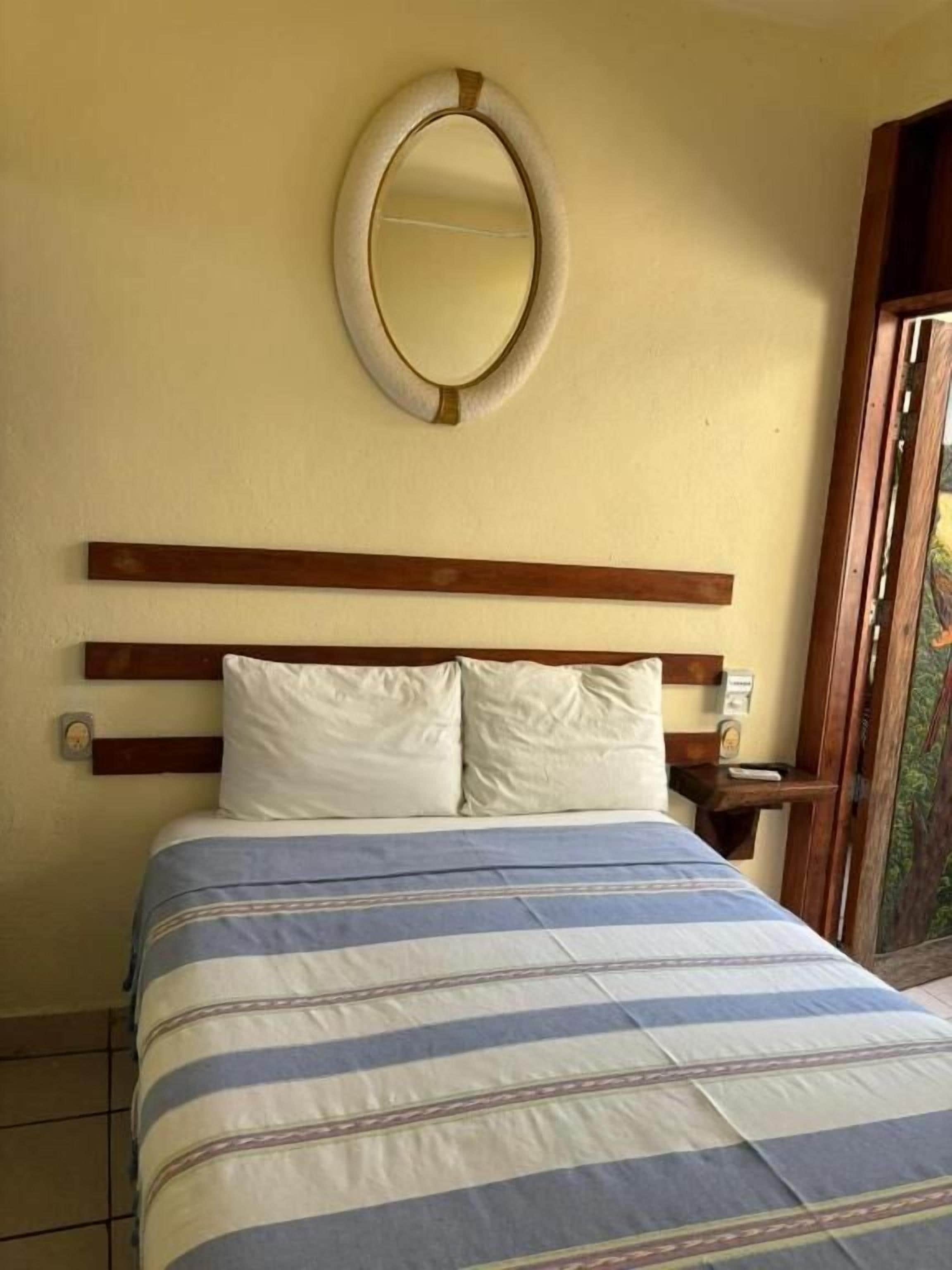 A bed with a striped bedspread, a wooden headboard, and a round mirror on the wall.