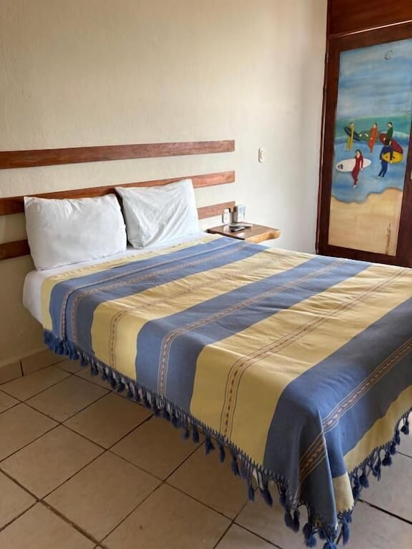 A bed with a striped blanket, a wooden headboard, a nightstand with a lamp, and a painting on the wall. - Casa piedra parada hotel (Brisas de Zicatela)