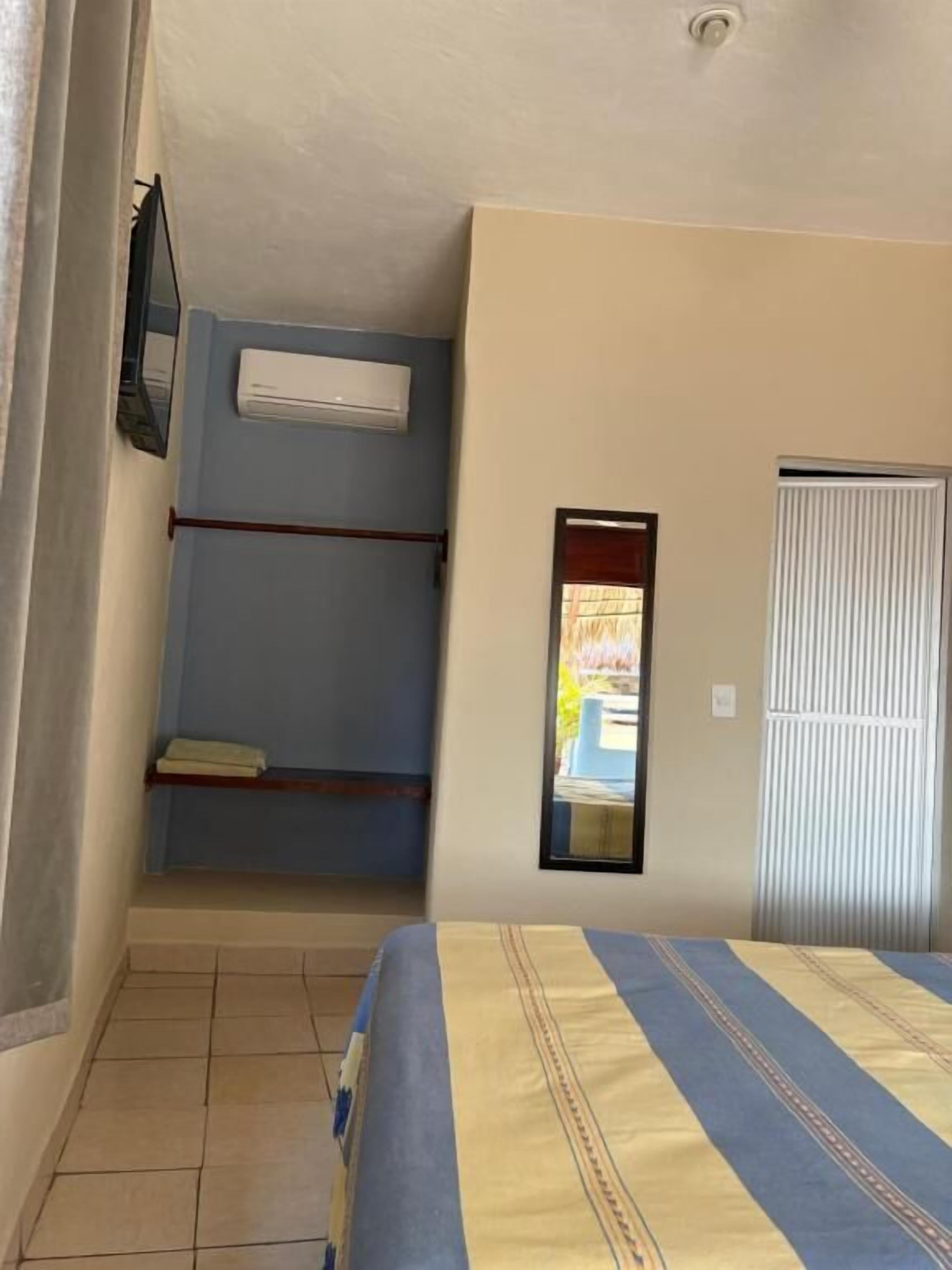A bedroom with a bed, an air conditioning unit, a window, and a door.