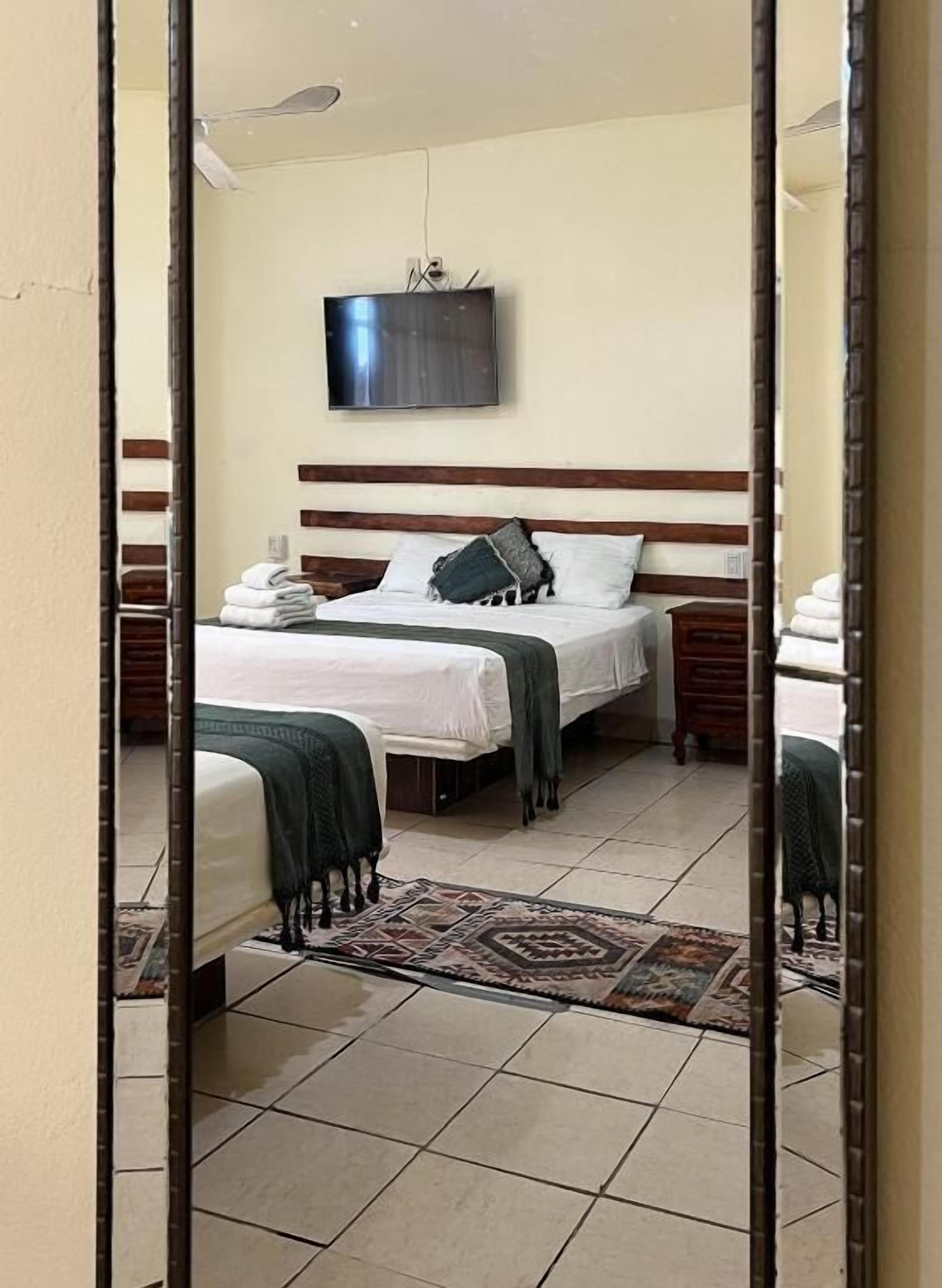 Une chambre d’hôtel avec deux lits, un téléviseur à écran plat, une tête de lit en bois et un tapis à motifs.