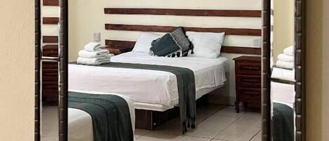 Une chambre d’hôtel avec deux lits, un téléviseur à écran plat, une tête de lit en bois et un tapis à motifs.