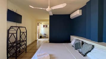 Habitación de hotel con cama, ventilador de techo, televisor montado en la pared y aire acondicionado.