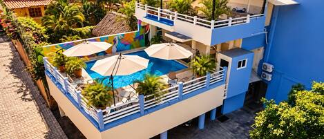 A multi-level building with a rooftop pool area, surrounded by potted plants and outdoor furniture.