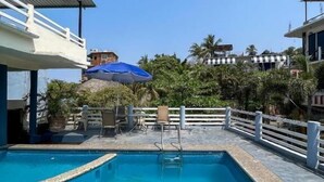 Una piscina con cerca blanca, sillas de descanso y sombrillas.