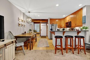 A modern kitchen with wooden cabinets, a stainless steel refrigerator, and a bar area with stools. - Dobie 26 with Wintergreen Advantage (Wintergreen)