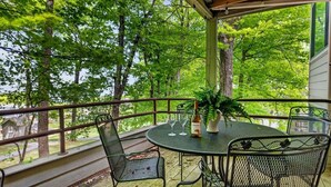Uma área externa coberta com uma mesa redonda e cadeiras, delimitada por um corrimão e com vista para uma área arborizada.