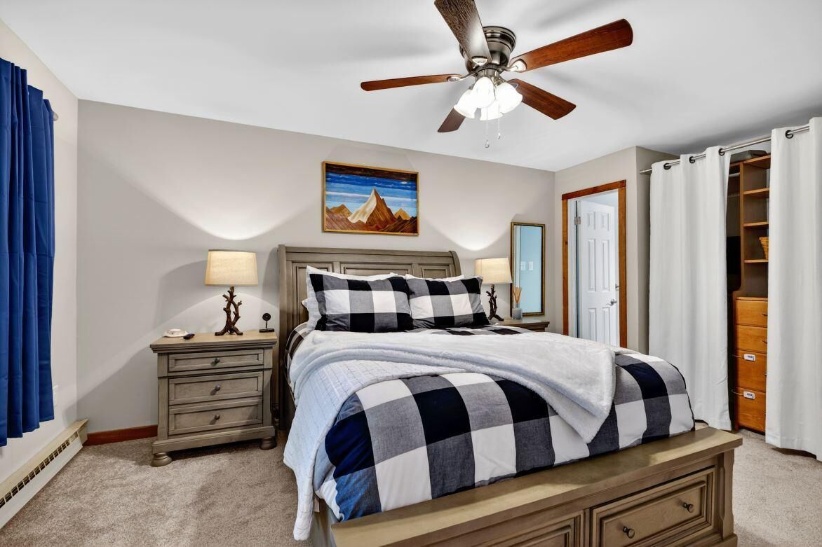 A bedroom with a bed, a nightstand, a lamp, a ceiling fan, a painting, and a closet.