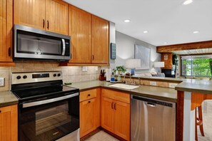 A modern kitchen with wooden cabinets, stainless steel appliances, and a large window providing natural light. - Dobie 26 with Wintergreen Advantage (Wintergreen)