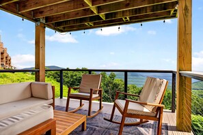 Eine Holzterrasse mit einer Couch und zwei Schaukelstühlen, mit Blick auf eine üppige, grüne Landschaft.