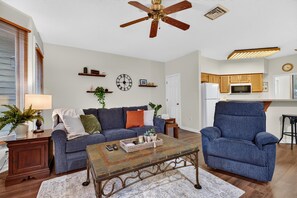 Ein Wohnzimmer mit Sofa, Sesseln, Couchtisch und Deckenventilator.