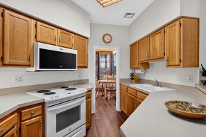 A modern kitchen with wooden cabinets, a built-in microwave, a stove, and a large island with a bowl. - Trillium Close 18 with Wintergreen Advantage (Wintergreen)
