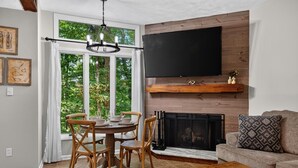 Ein Wohnzimmer mit Kamin, einem Esstisch mit Stühlen, einer Couch und einem an der Wand befestigten Fernseher.