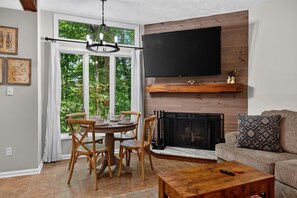 A living room with a fireplace, a dining table with chairs, a sofa, and a television mounted on the wall. - Laurelwood 00 with Wintergreen Advantage (Wintergreen)