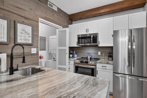 A modern kitchen with stainless steel appliances, a marble countertop, and wooden wall paneling. - Laurelwood 00 with Wintergreen Advantage (Wintergreen)