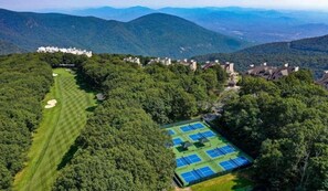 Luftaufnahme eines Golfplatzes mit Tennisplatz, umgeben von dichtem Wald und Wohngebäuden.