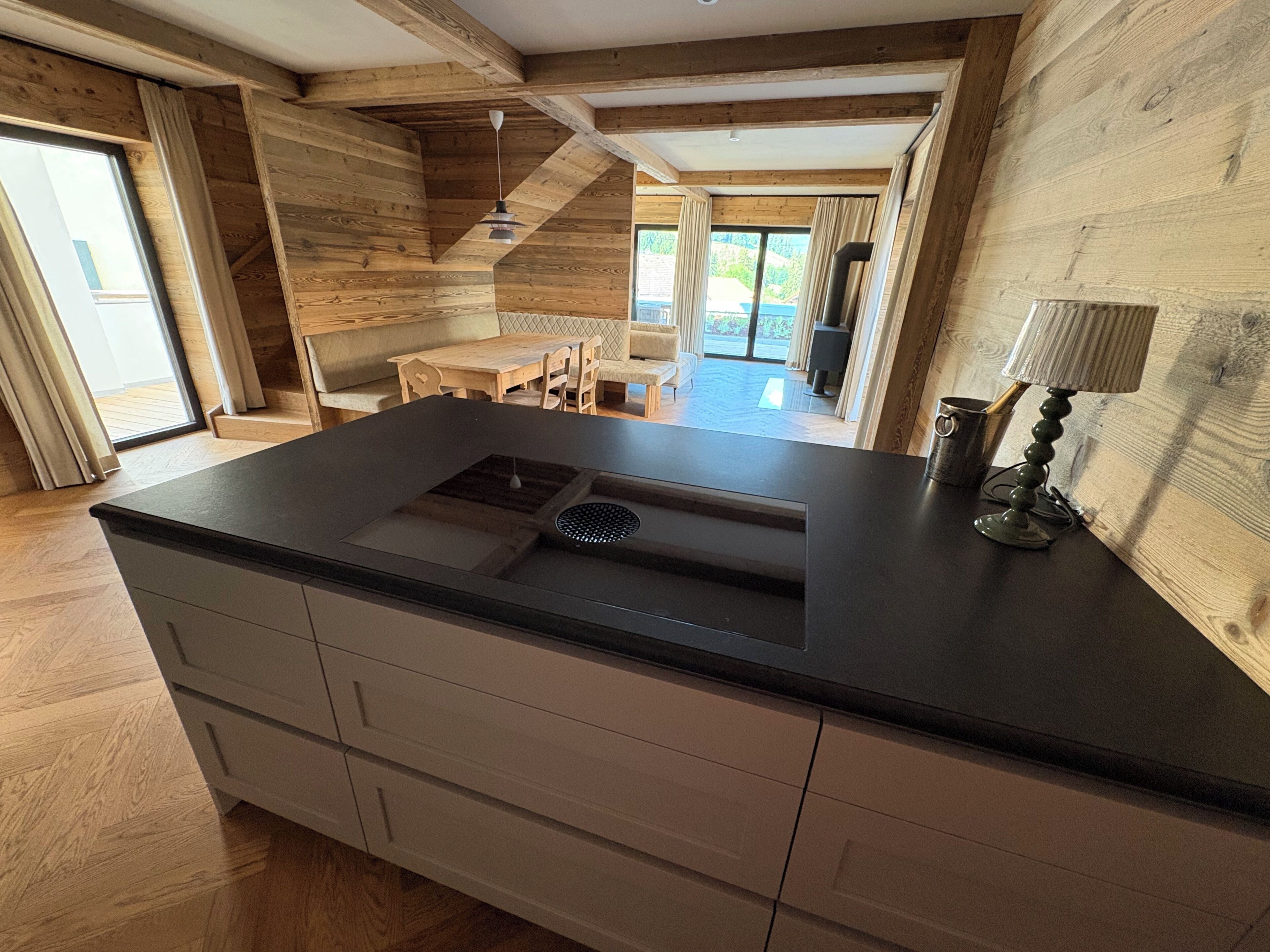 A modern kitchen with a central island, wooden beams, and a view to the dining area.