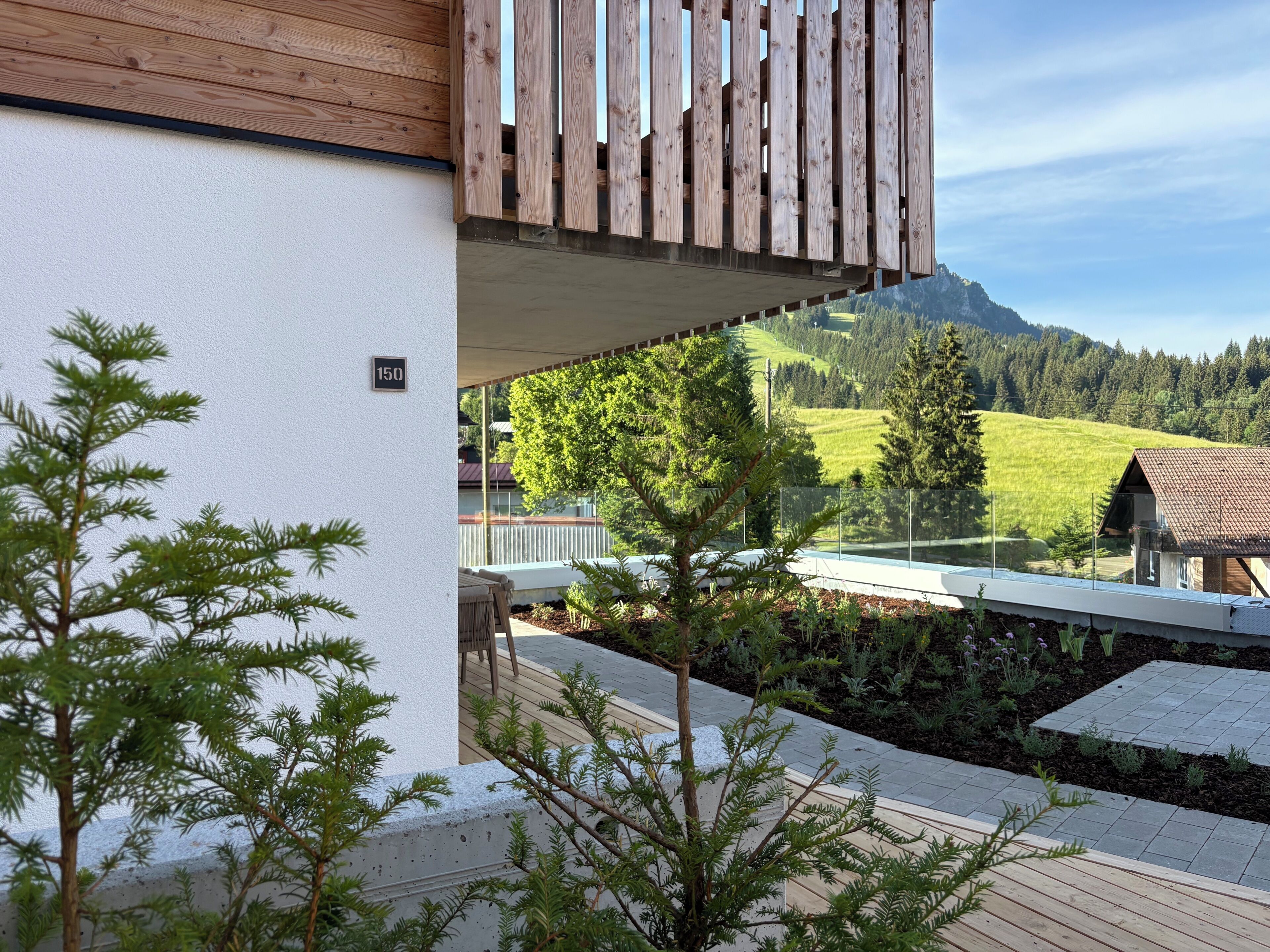 Een balkon met uitzicht op een berglandschap, een houten terras en een witte muur met een nummer.