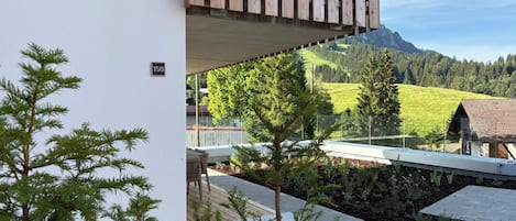 En balkon med udsigt over et bjerglandskab, en træterrasse og en hvid væg med et nummer på.