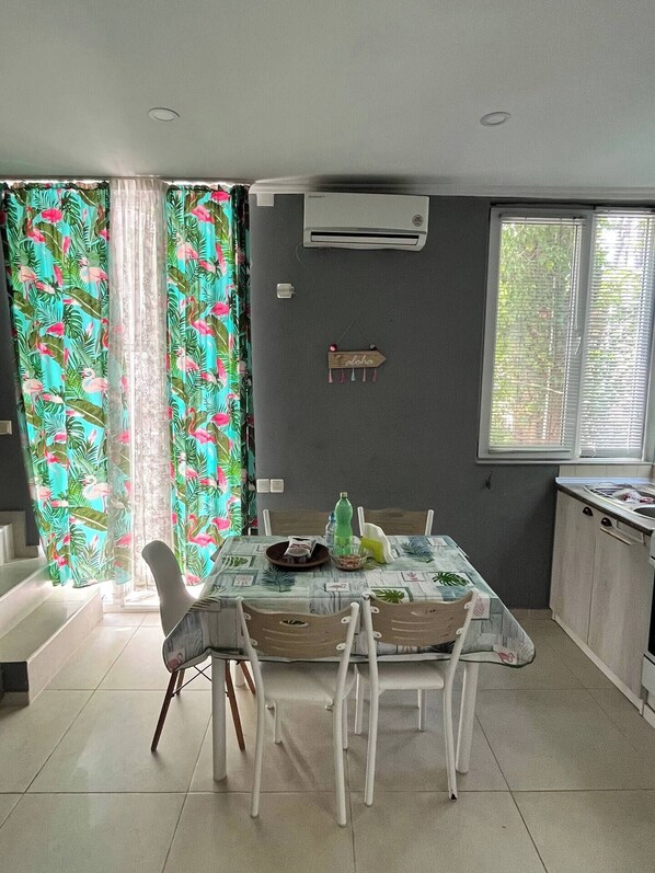 A dining area with a table set for four, a window with blinds, and an air conditioning unit on the wall.