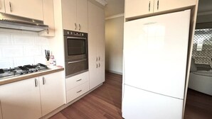 Eine moderne Küche mit weißen Schränken, einer Edelstahl-Dunstabzugshaube, einem eingebauten Backofen und einem weißen Kühlschrank.