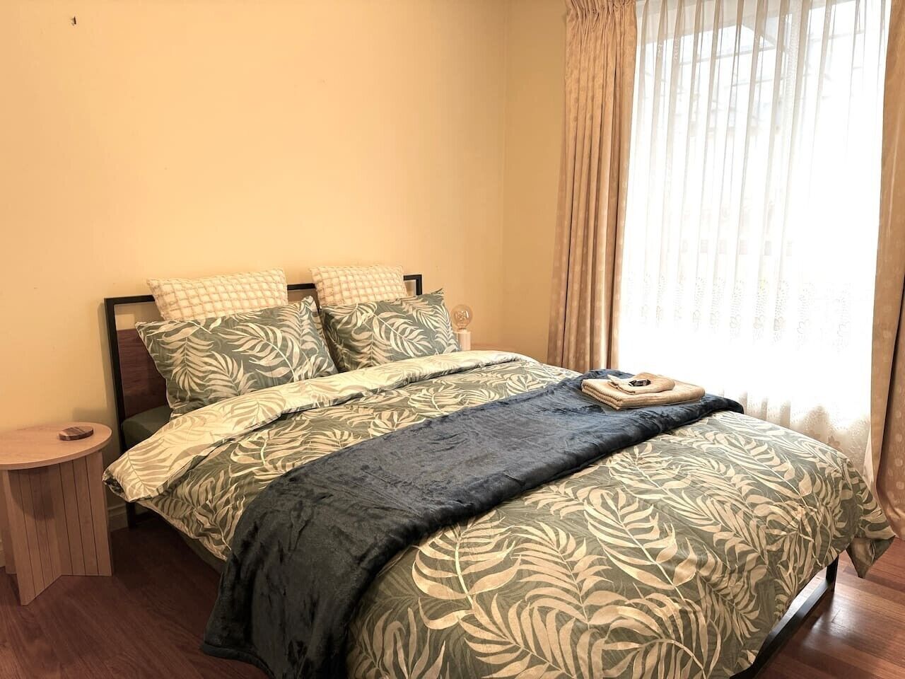 Un lit avec une couvre-lit à motifs de feuilles, une table de chevet et une fenêtre avec des rideaux.