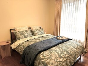 A bed with a leaf-patterned bedspread, a bedside table, and a window with curtains.