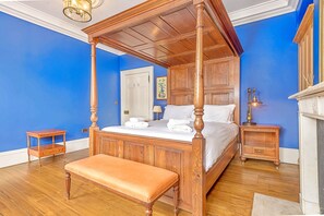 Ein Bett mit Baldachin, ein Holzkopfteil, eine Bank, ein Nachttisch und ein Beistelltisch mit Lampe.