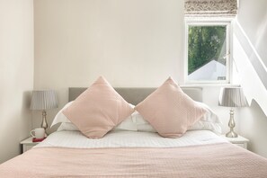 A neatly made bed with a white and pink bedding set, two bedside lamps, and a window with a view of greenery outside. - Peaceful Retreat With Welcome Tray (Ambleside)