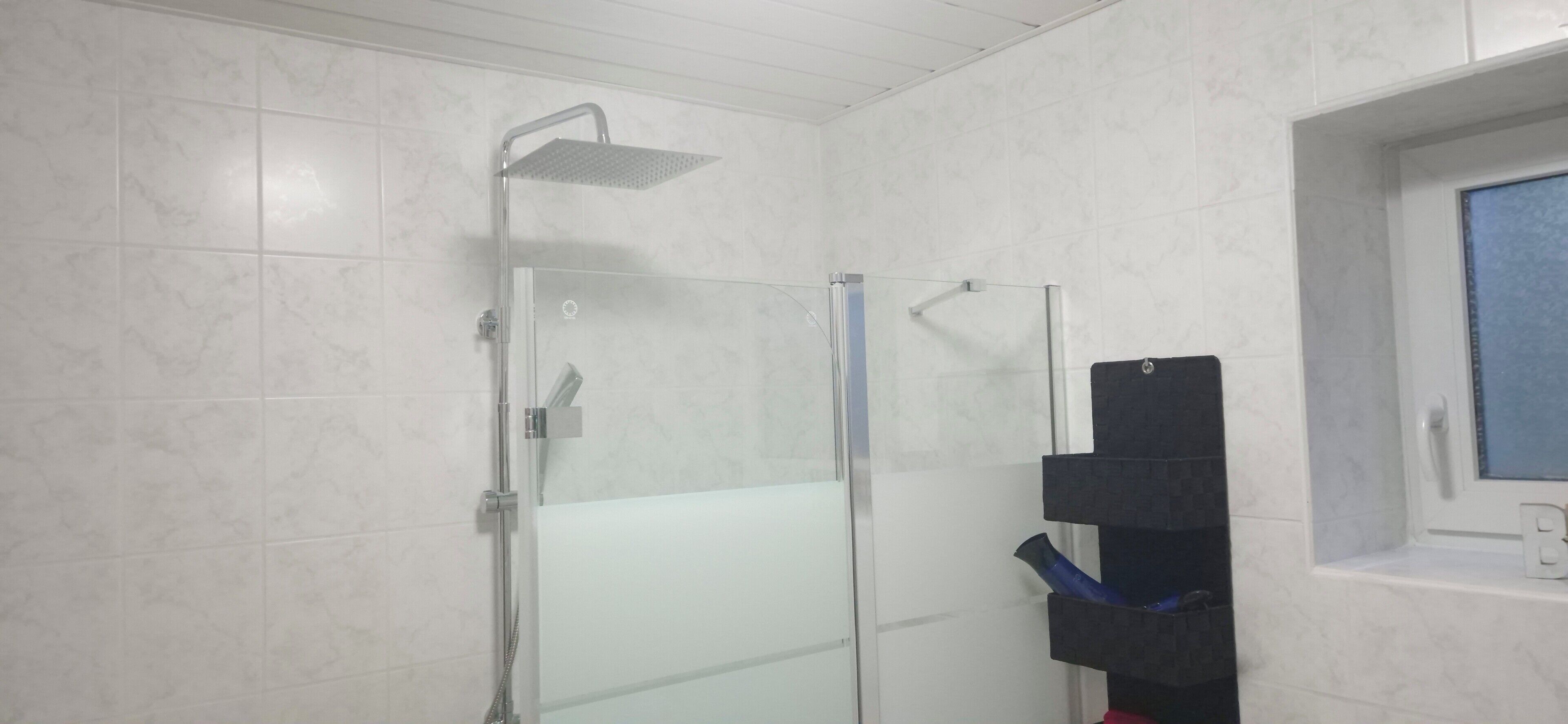A bathroom with a glass-enclosed shower, a white tiled wall, and a window with a view.