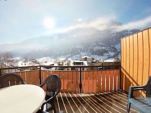 Eine Holzterrasse mit Tisch und Stühlen mit Blick auf eine verschneite Berglandschaft.