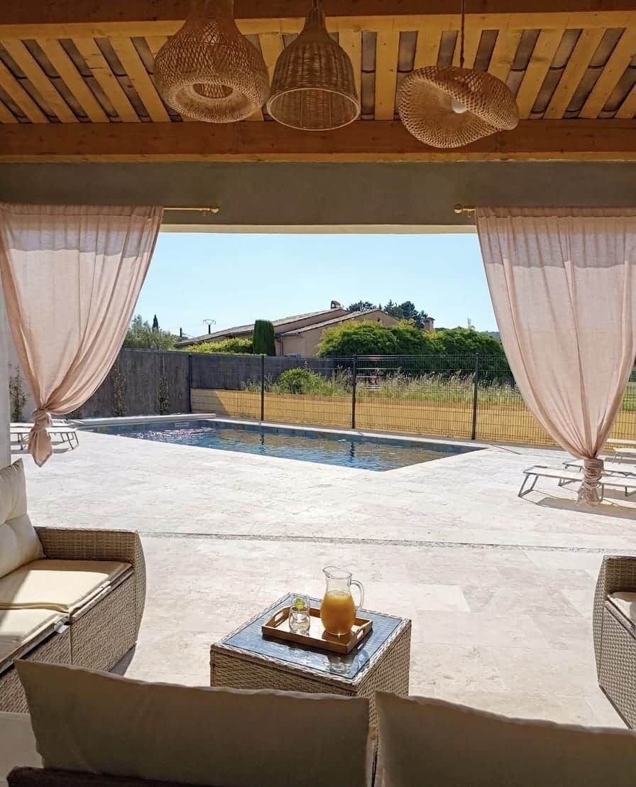 Un espace extérieur aménagé avec des meubles en osier, une table avec une carafe et des verres, et une vue sur une piscine et un paysage verdoyant.