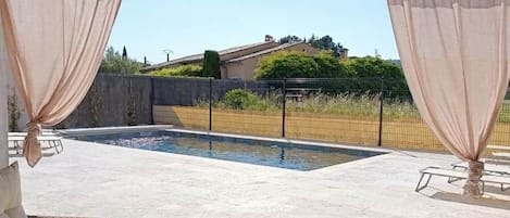 An outdoor seating area with wicker furniture, a table with a pitcher and glasses, and a view of a swimming pool and landscape.