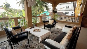 Un balcon avec un sol à motifs, un canapé, deux fauteuils, une table et des plantes suspendues.