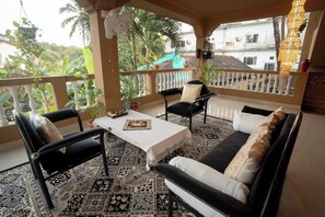 A balcony with a patterned floor, a sofa, two chairs, a table, and hanging plants. - Hill view apartment 2 (Ashwem)