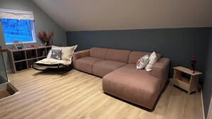 Ein modernes Wohnzimmer im Loft-Stil mit einem großen Ecksofa, einem kleinen Holztisch und einem Fenster mit Blick auf Bäume.
