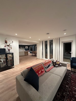 Een moderne woonkamer met een bank, een glazen kast en een keuken op de achtergrond.