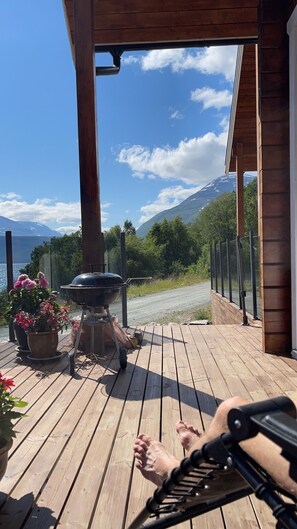 Eine Holzterrasse mit Grill, Blumentöpfen und Blick auf einen Berg.