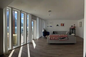 Ein großzügiger Wohnbereich mit Sofa, Couchtisch, großen Fenstern mit Blick und einem Balkon.