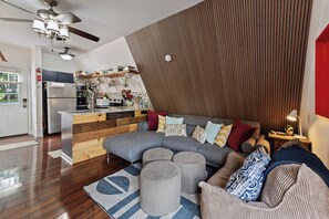 A modern living room with a sectional sofa, ottomans, and a kitchen area with a wooden accent wall.