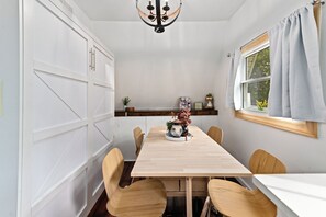 A dining area with a wooden table, chairs, a chandelier, and a window with curtains.